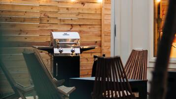 An outdoor patio with a grill, wooden chairs, and a table.