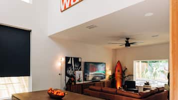 A modern living room with a dining area, featuring a large orange sign, a surfboard decoration, and a black and white patterned rug.