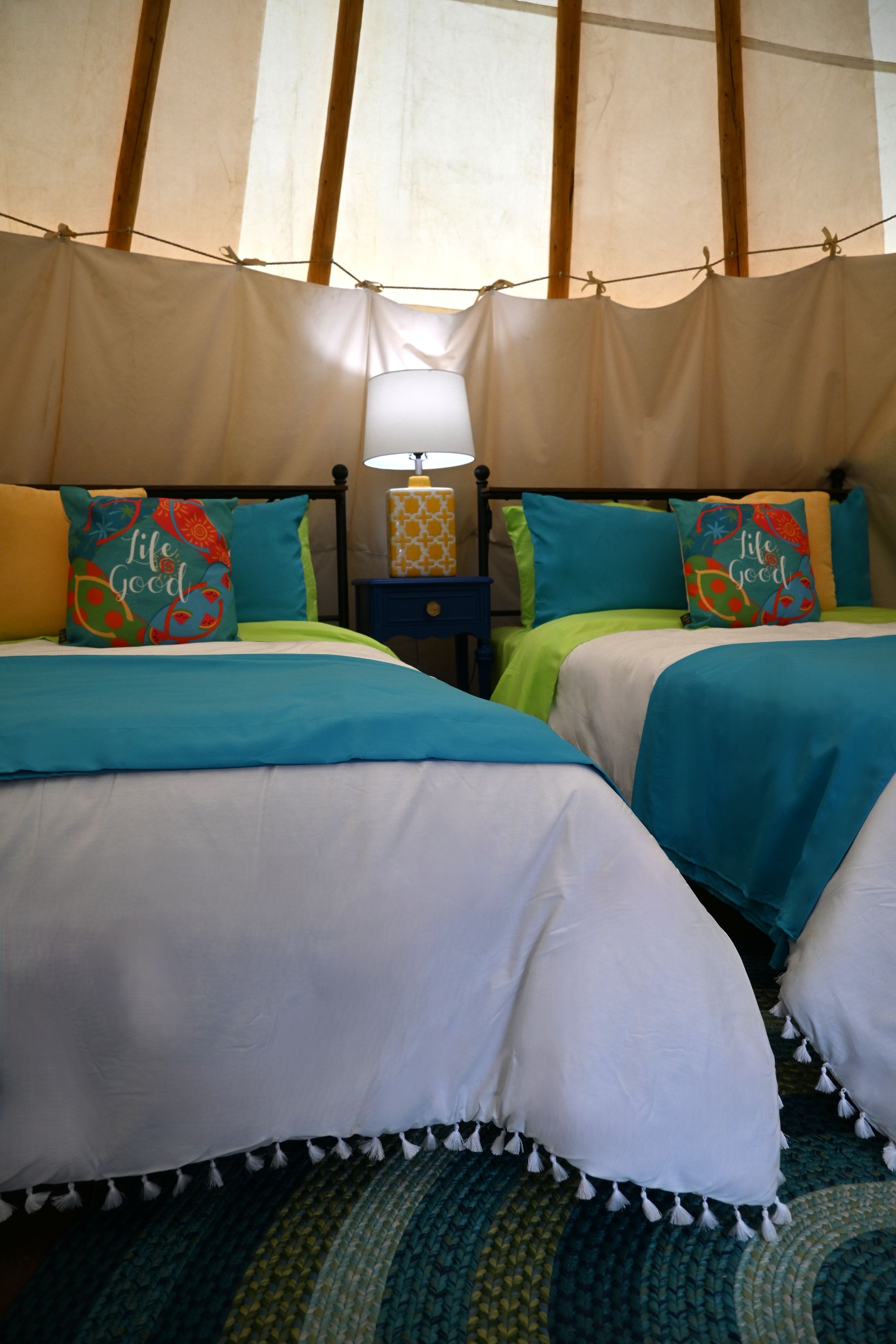 Una stanza a tenda con due letti, ciascuno con cuscino e comodino con lampada.