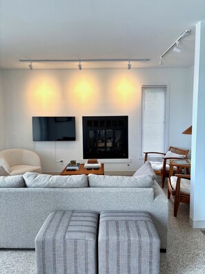 Ein modernes Wohnzimmer mit einer großen Eckcouch, einem flachbildfernseher an der Wand, einem Kamin und einem Essbereich mit Holzsesseln und einem Tisch.