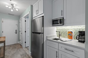 A modern kitchen with white cabinets, a stainless steel refrigerator, a microwave, and a coffee maker. - Tops'l Summit106A•NewRemodel•Pool+HotTub•BeachGear (Miramar Beach)