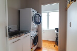 Une petite buanderie comprenant un lave-linge et un sèche-linge, un petit évier et une fenêtre qui laisse entrer la lumière naturelle.