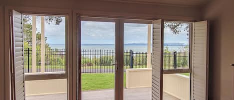 A room with a sliding glass door leading to a balcony with a view of a body of water and mountains.
