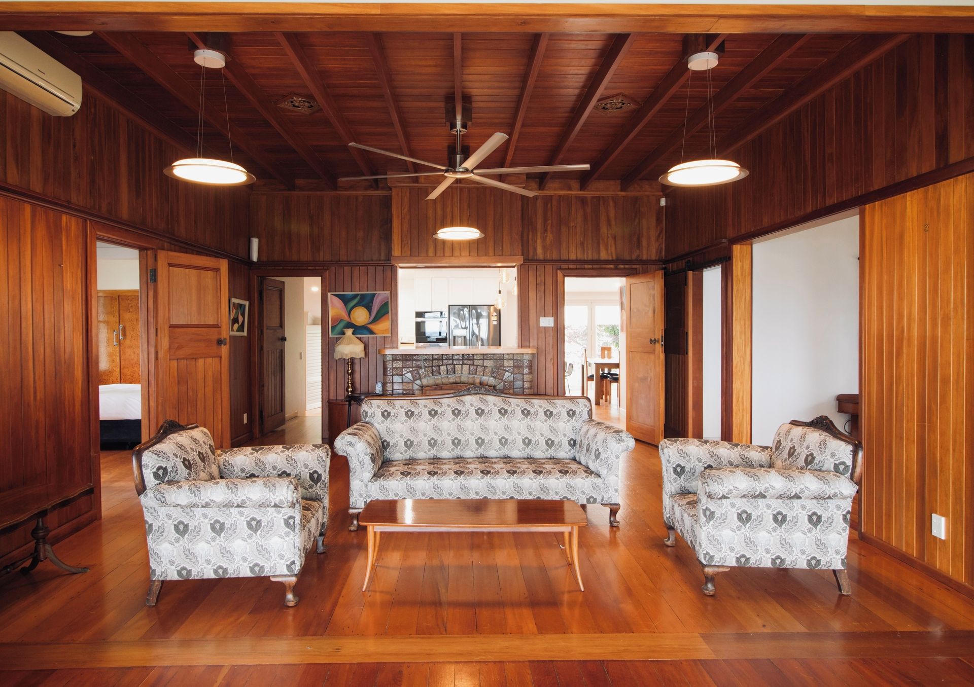 A spacious living room with wooden paneling, a central sofa set, and a ceiling fan.