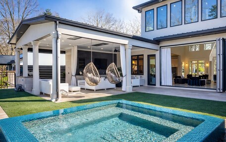 A modern house with a covered outdoor seating area, a swimming pool, and a large glass door leading to a spacious interior.