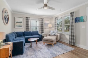 A living room with a blue sofa, a small round table, a beige armchair, and a ceiling fan. - Old Oak Oasis|Hot Tub·Golf Cart·Fire Pit·MHC (Morehead City)