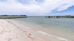 Een strand met een houten pier die zich uitstrekt over kalm water, een zandstrand en een heldere lucht.