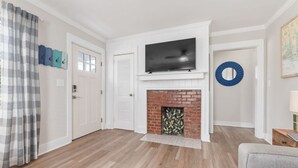 Een woonkamer met een open haard, een flatscreen televisie erboven en een deur met raam.