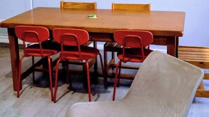 Una sala de conferències amb una taula de fusta, cadires vermelles i una cadira amb coixí beix. Hi ha dos quadres penjats a la paret.