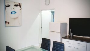 Una habitació amb una taula de vidre, dues cadires negres, un armari blanc i un televisor de pantalla plana gran.