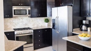 Een moderne keuken met donkere kastjes, een roestvrijstalen koelkast, een magnetron en een gasfornuis.