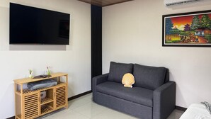 Uma sala de estar moderna com um sofá cinzento, um móvel de TV de madeira e um quadro na parede.