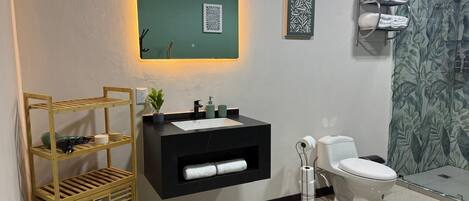 A bathroom with a black sink, white toilet, and a wooden shelf unit.
