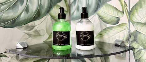 A bathroom with a glass shelf holding two bottles of Arenal Star Studios shampoo and conditioner.