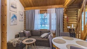 A cozy log cabin interior with a wooden ceiling, a gray sofa, a small round table, and a dining table with placemats. - Levin ainola by Interhome (Kittilä)