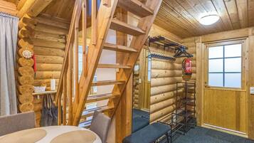 A log cabin interior with a wooden staircase, a dining table, and a fire extinguisher mounted on the wall.