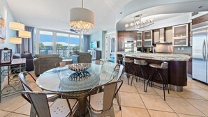 Een moderne keuken met een centraal eiland, barstoelen en een eethoek met een glazen tafel en stoelen.