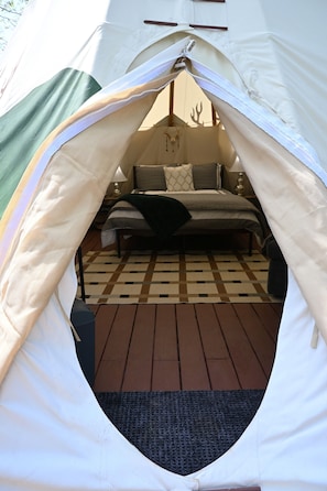A tent with a bed inside, a checkered floor, and a lamp on a bedside table.