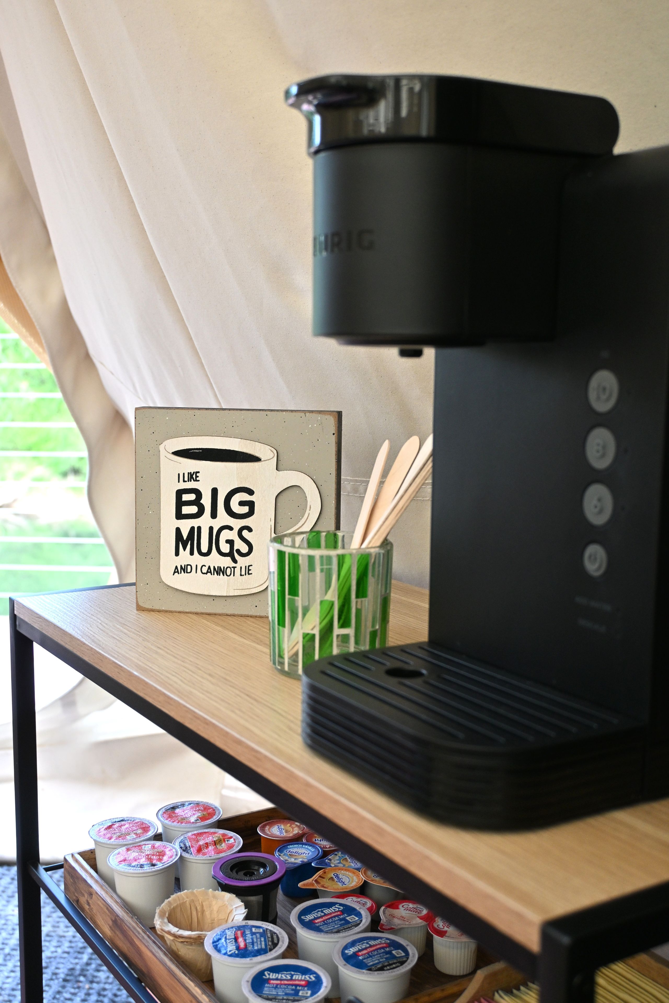 A coffee maker, a mug sign, and a container with utensils on a table.