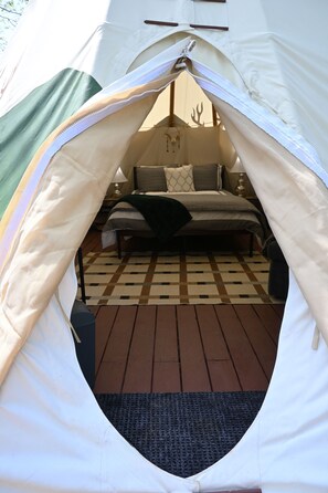 A tent with a bed inside, a checkered floor, and a lamp on a bedside table.