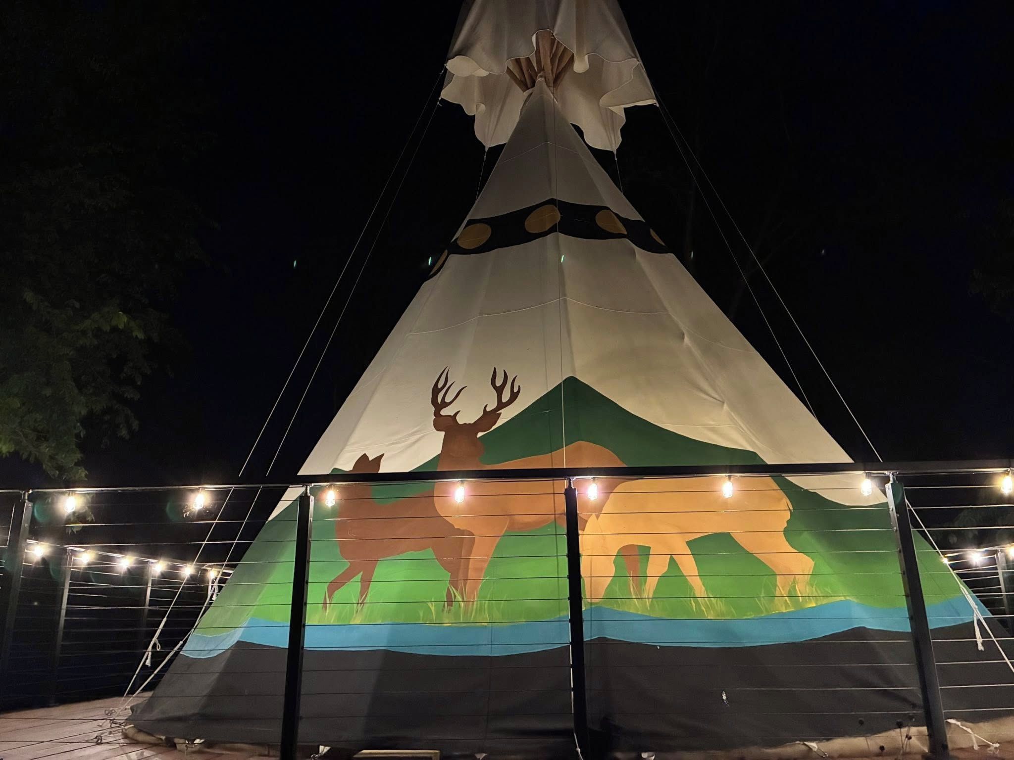 Une grande tente amérindienne illuminée, décorée de peintures représentant un bison et des montagnes.