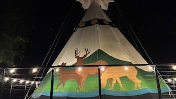 A large, illuminated tipi with a painted buffalo and mountain design.