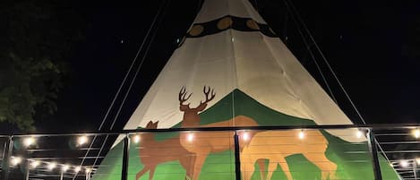 A large, illuminated tipi with a painted buffalo and mountain design.