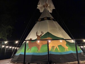 Uma tenda tipi grande, iluminada, com pintura de um búfalo e montanhas.