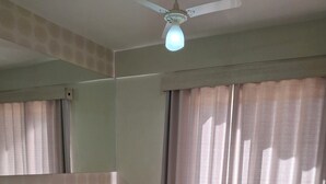 Une chambre d’hôtel avec un lit, un bureau, une chaise et un ventilateur de plafond.