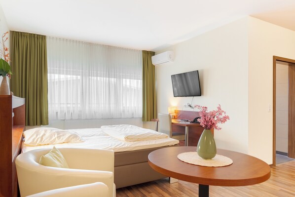 Habitación de hotel con cama, escritorio, silla, televisor y un jarrón con flores.