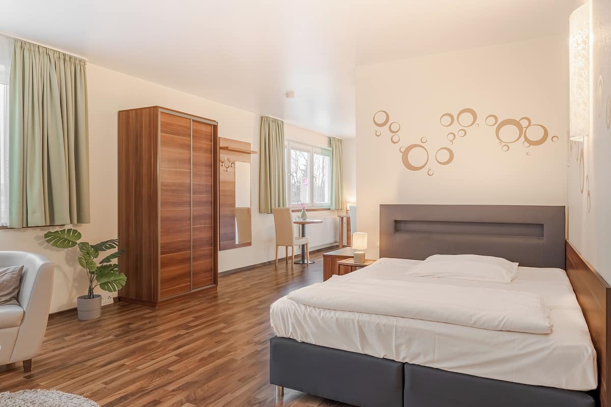 A modern hotel room with a large bed, a desk, a chair, and a wardrobe.