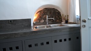 A kitchen with a stone arch wall, a stainless steel sink, and a modern faucet. - Christina's Cave House (Santorini)