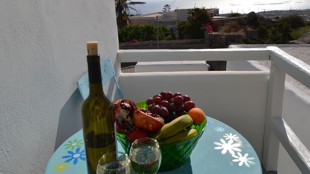 A balcony with a table set for two, featuring a bottle of wine, two glasses, and a bowl of fruit. - Christina's Cave House (Santorini)