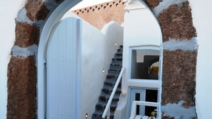 A narrow hallway with a white door and a staircase leading to a room with a white sink and a small window. - Christina's Cave House (Santorini)