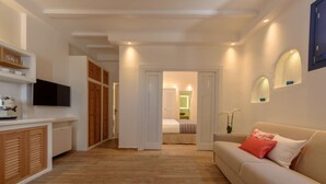 A modern living room with a sofa, a television, and a kitchen area with cabinets and a microwave. - Sea Dream (Santorini)