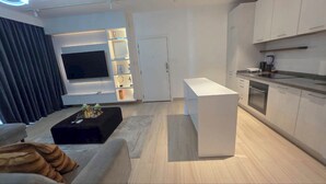 Un salon moderne doté d’un téléviseur à écran plat, d’un canapé, d’une table basse et d’un coin cuisine avec des placards et des appareils électroménagers.