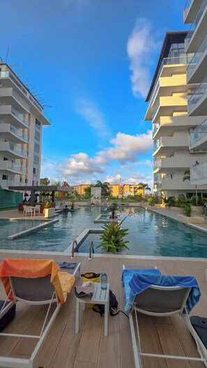Un espace piscine avec des chaises longues et une petite table, entouré d’immeubles dotés de balcons.