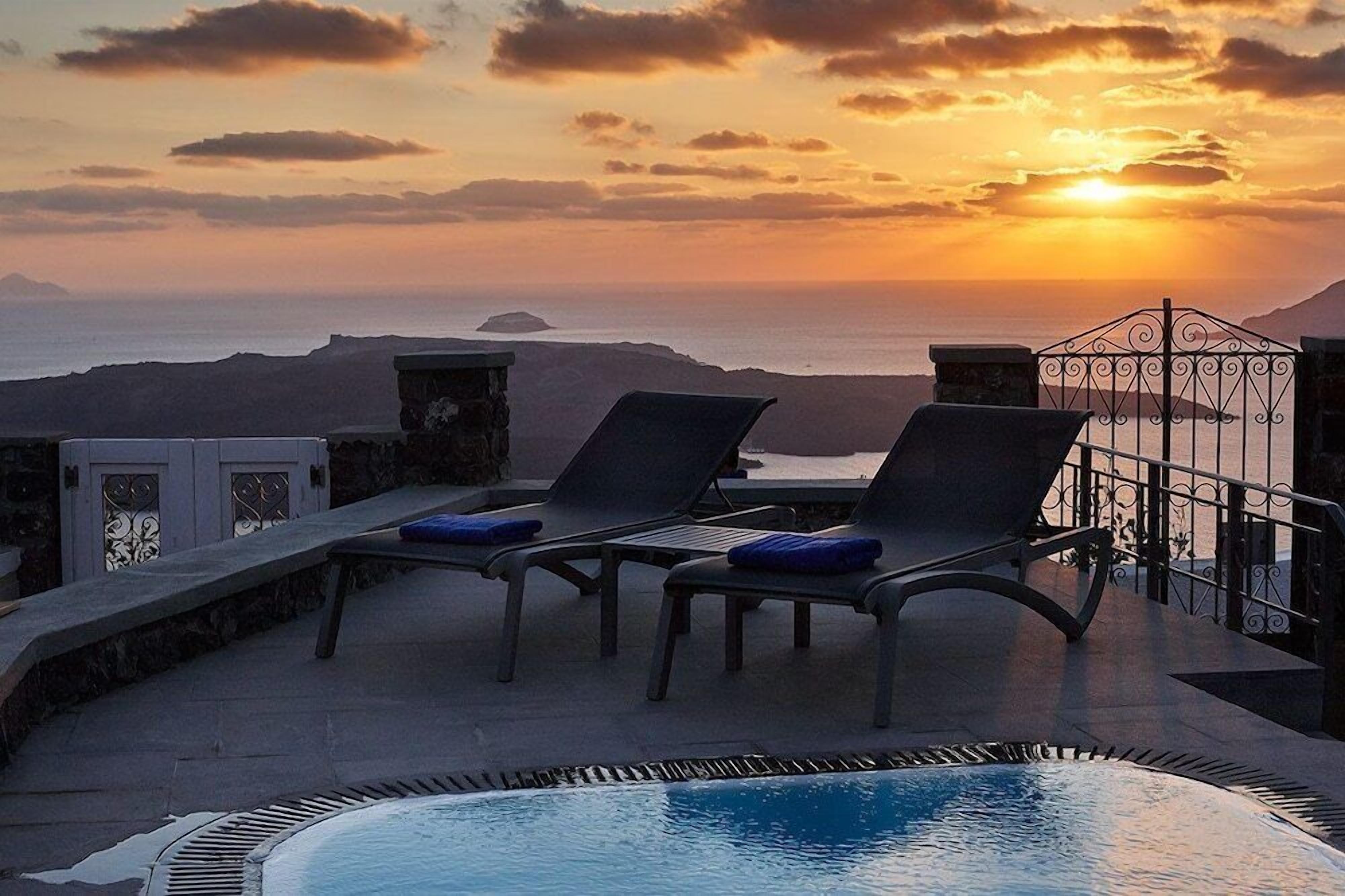 A poolside area with lounge chairs and a view of the sunset over the sea.