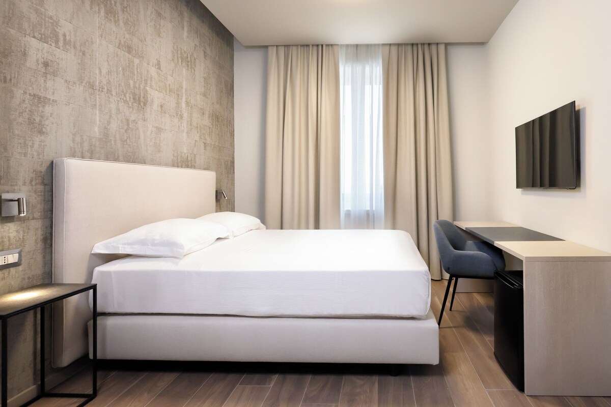 A modern hotel room with a bed, a desk, and a television.