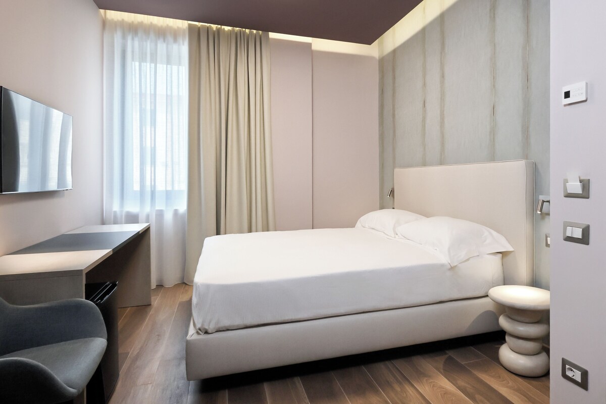 A hotel room with a bed, a desk, a chair, and a television.