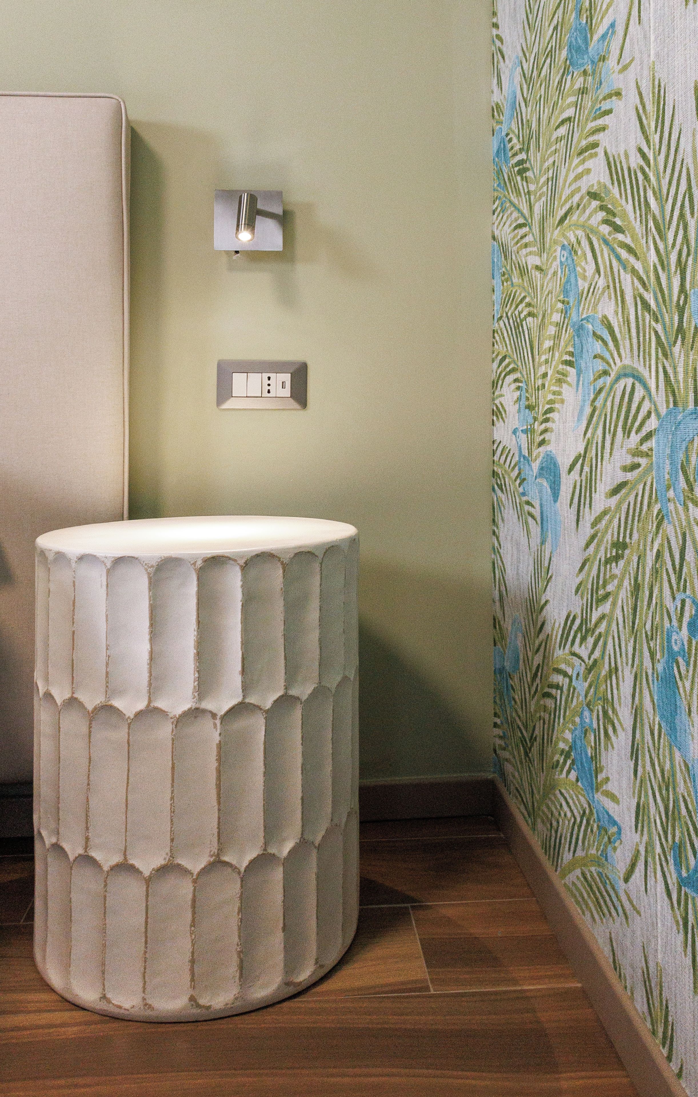 Une salle de bain avec un lavabo rond à surface texturée, un luminaire fixé au mur et un papier peint à motifs.