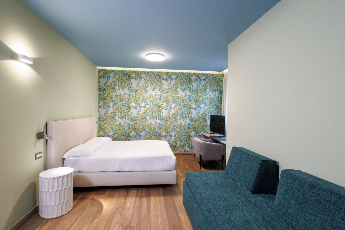 A hotel room with a bed, a sofa, a small table, and a TV.