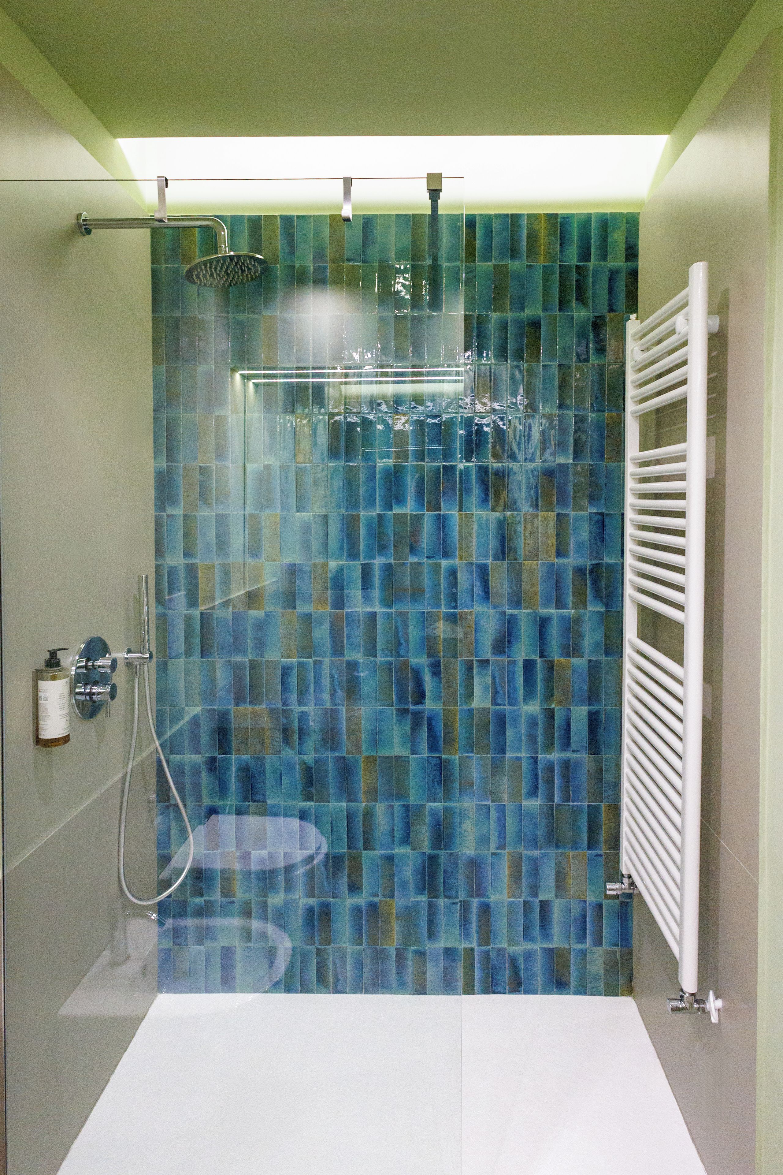 A shower with a glass door, a white towel rack, and a wall-mounted heater.
