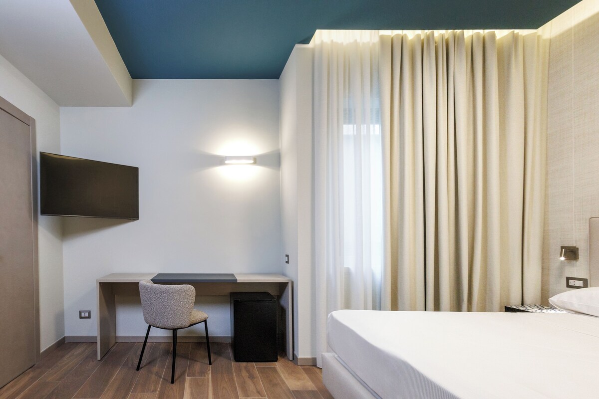 A hotel room with a bed, a desk, a chair, a television, and curtains.
