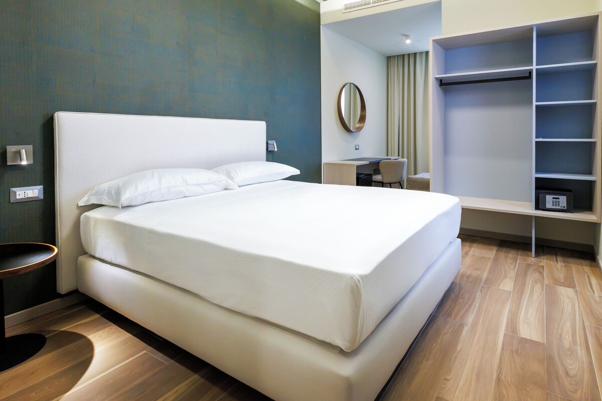 A hotel room with a large bed, a desk, and a wardrobe.