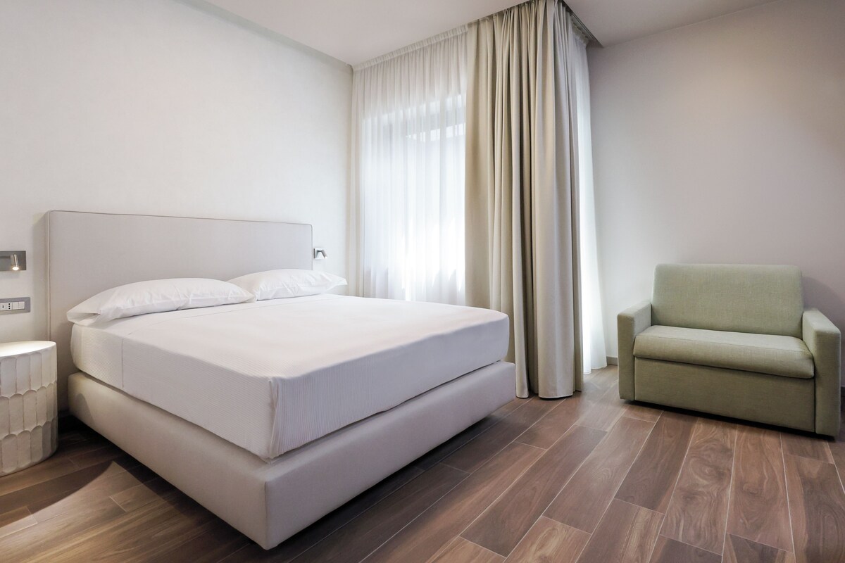 A hotel room with a large bed, a chair, and a window with curtains.