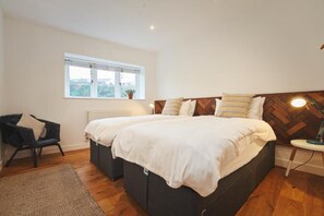 A bedroom with two beds, a window, a radiator, a chair, and a lamp. - The Crabshell (Kingsbridge)