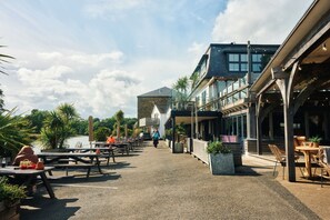 An outdoor seating area with tables and chairs, a building with a stone facade, and a view of the water. - The Crabshell (Kingsbridge)