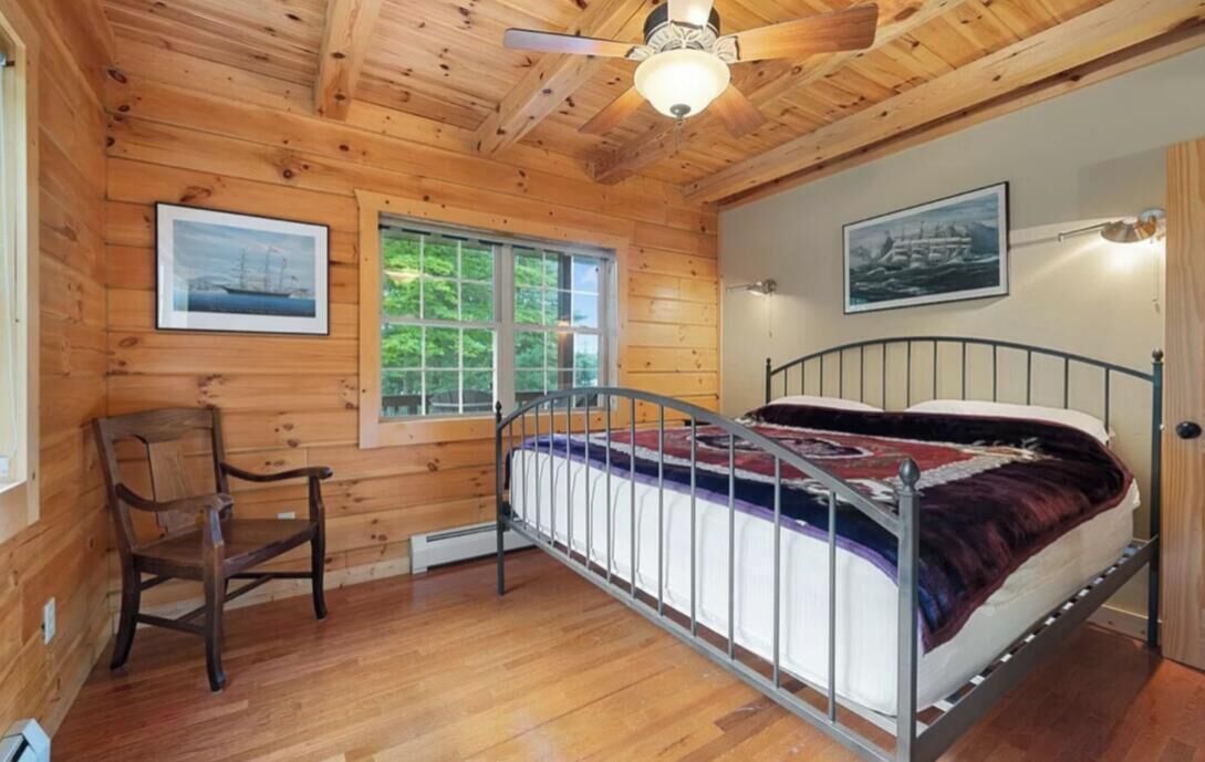 A wooden cabin bedroom with a metal bed frame, a wooden chair, and two framed pictures on the walls.