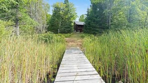A wooden boardwalk leading to a cabin surrounded by tall grass and trees. - Enjoyable 4-bedroom cabin with AC in Niagara, on a private 56 acre lake (Niagara)